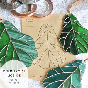 May include: Three green stained glass fig leaf ornaments with copper wire accents. The leaves are hanging from brown cords. The image also includes a pattern for making the leaves and copper foil tape.