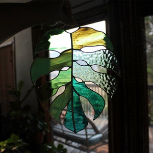 Peut inclure: Une fen&ecirc;tre en verre color&eacute; suspendue, repr&eacute;sentant une feuille de monstera verte et jaune.