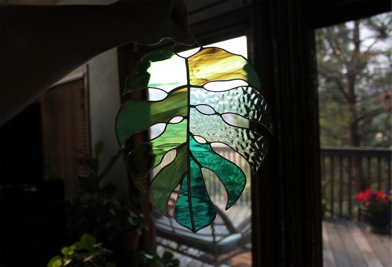 Peut inclure: Une fen&ecirc;tre en verre color&eacute; suspendue, repr&eacute;sentant une feuille de monstera verte et jaune.