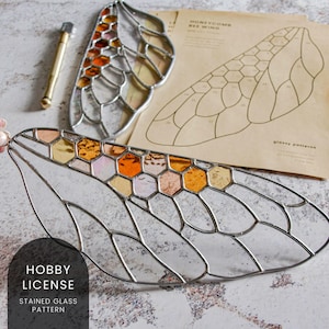 May include: A stained glass bee wing pattern with a honeycomb design. The pattern is made of clear, amber, and peach glass. The pattern is on a white background. The text "Hobby License Stained Glass Pattern" is visible in the image.