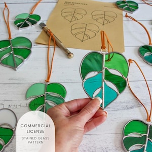 May include: A set of stained glass monstera leaf ornaments with a brown leather cord. The leaves are green, blue, and white. The image includes the text "COMMERCIAL LICENSE STAINED GLASS PATTERN".