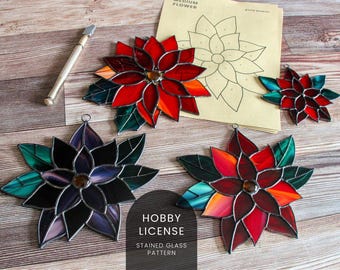 Könnte beinhalten: Buntglas-Weihnachtsstern-Ornamente in Rot-, Orange- und Lilatönen mit grünen Blättern. Ein Glasschneider und eine Vorlage für eine mittelgroße Blume sind ebenfalls vorhanden. Die Ornamente haben eine Metallschlaufe zum Aufhängen. Der Text "HOBBY LICENSE STAINED GLASS PATTERN" ist sichtbar.