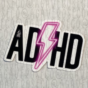 May include: A black and white sticker with the text "ADHD" in a bold font. A pink lightning bolt is behind the text.