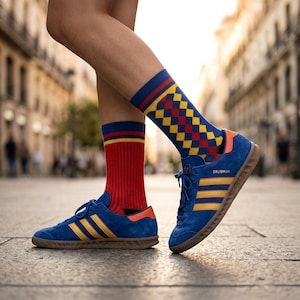May include: A person wearing blue suede trainers with yellow stripes and red and blue socks. One sock is red with yellow stripes, and the other is blue with a yellow, red, and blue checkered pattern. The shoes have brown soles.