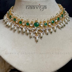 K&ouml;nnte beinhalten: Eine goldene und gr&uuml;ne Halskette mit wei&szlig;en Perlen und smaragdgr&uuml;nen Steinen. Die Halskette befindet sich auf einer wei&szlig;en Mannequin-B&uuml;ste. Der Text "naaviya" ist im Bild sichtbar.