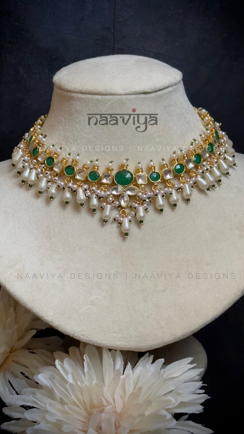 K&ouml;nnte beinhalten: Eine goldene und gr&uuml;ne Halskette mit wei&szlig;en Perlen und smaragdgr&uuml;nen Steinen. Die Halskette befindet sich auf einer wei&szlig;en Mannequin-B&uuml;ste. Der Text "naaviya" ist im Bild sichtbar.