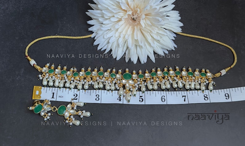 K&ouml;nnte beinhalten: Eine goldene Choker-Halskette mit gr&uuml;nen und wei&szlig;en Steinen und Perlen-Tropfen. Die Halskette ist 12,7 cm lang und wird mit passenden Ohrringen geliefert. Die Ohrringe haben gr&uuml;ne und wei&szlig;e Steine und Perlen-Tropfen.