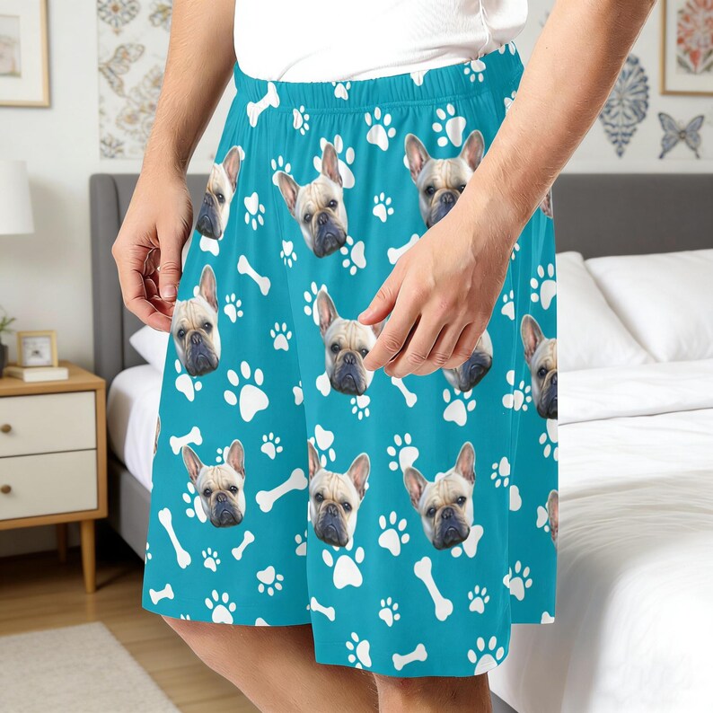 K&ouml;nnte beinhalten: Hellblaue Shorts mit einem sich wiederholenden Muster aus franz&ouml;sischen Bulldoggen-Gesichtern, wei&szlig;en Pfotenabdr&uuml;cken und wei&szlig;en Knochenformen. Die Shorts haben einen elastischen Bund und eine lockere Passform mit leuchtenden Farben.