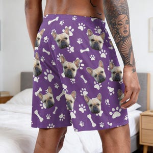 K&ouml;nnte beinhalten: Violette Shorts mit einem sich wiederholenden Muster aus cremefarbenen Hunde-Pfotenabdr&uuml;cken, wei&szlig;en Knochen und den Gesichtern rehfarbener Franz&ouml;sischer Bulldoggen. Die Shorts haben einen elastischen Bund und eine lockere Passform.