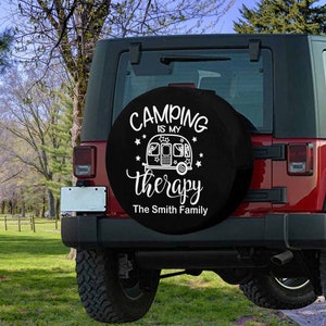 May include: Black spare tire cover with white text that reads "Camping is my therapy The Smith Family". The cover features a white silhouette of a camper trailer with stars.