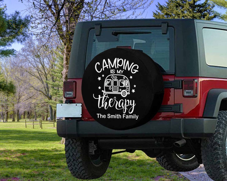 May include: Black spare tire cover with white text that reads "Camping is my therapy The Smith Family". The cover features a white silhouette of a camper trailer with stars.