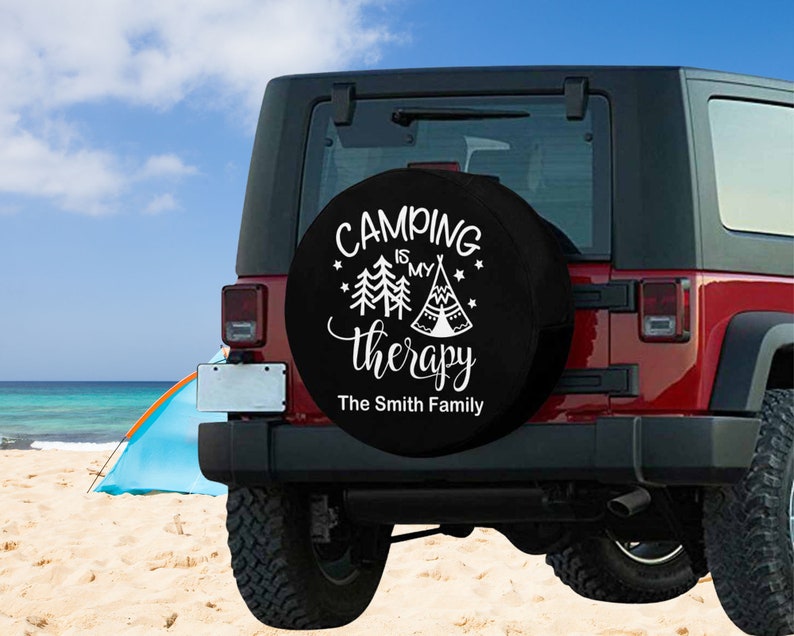 May include: Black spare tire cover with white text that reads "Camping is my therapy" with a stylized image of a tent and trees. The text "The Smith Family" is below the main text.