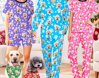 May include: Three sets of pajamas featuring a repeating pattern of dog faces and white paw prints. One set is purple with shorts, one is blue with long sleeves and pants, and one is pink with pants. Two dogs are in front wearing matching bandanas.