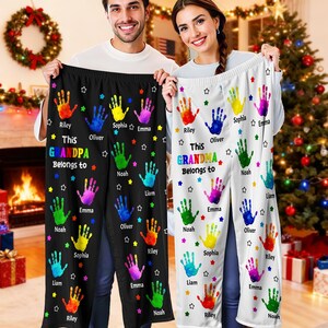May include: Black and white personalized pajama pants with colorful handprints and names. The text reads "This Grandpa Belongs to" and "This Grandma Belongs to". A unique gift for grandparents.