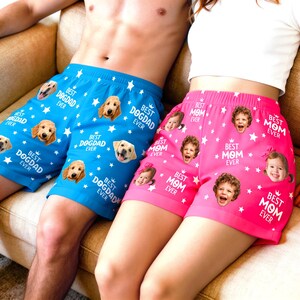 May include: A pair of blue shorts featuring a repeating pattern of dog faces and the text BEST DOGDAD EVER with white stars, and a pair of pink shorts featuring a repeating pattern of children's faces and the text BEST MOM EVER with white stars.