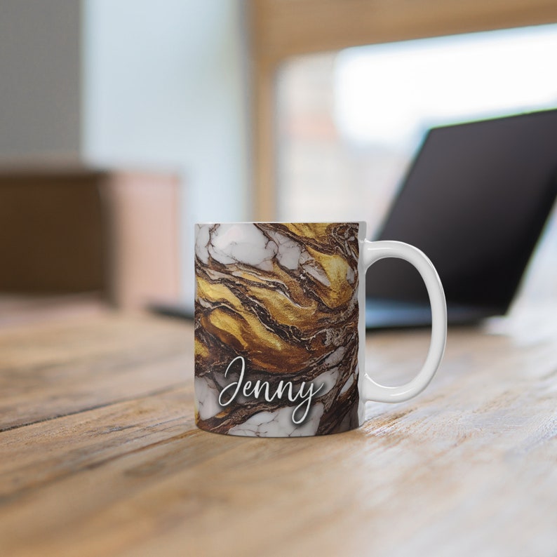 May include: White ceramic mug with a gold and brown marble design. The mug has the name "Jenny" written on it in white cursive.