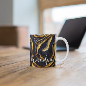 May include: White ceramic mug with a black and gold marbled design. The mug has a white handle and the word "Grandpa" written in white script on the front.