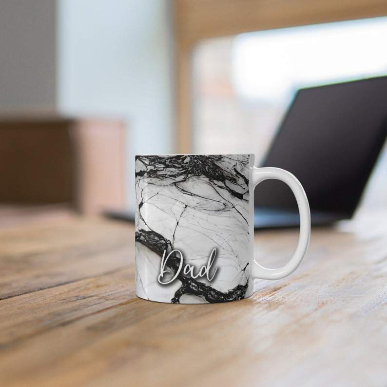 May include: White ceramic mug with a black and white marble pattern and the word "Dad" in a cursive font.