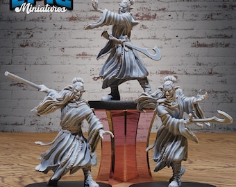 May include: Three gray painted miniature figurines of elves wearing robes and holding weapons. The figures are posed in dynamic stances and are set on black bases. The figures are from the Epic Miniatures brand.