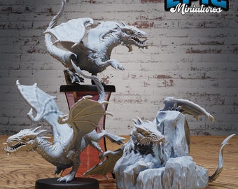 May include: Three gray, unpainted dragon miniatures in various poses. The dragons are posed on a wooden surface with a brick wall in the background. The text "EPIC Miniatures" is visible in the upper right corner of the image.