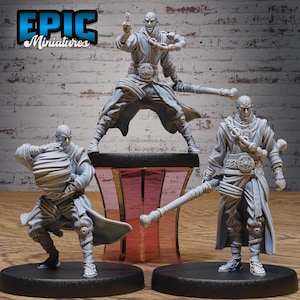 May include: Three gray miniature figurines of a bald warrior in action poses. The figurines are on black bases, with one standing on a pink and black stand. The figurines are holding weapons and wearing detailed clothing. The text "EPIC Miniatures" is in the top left corner.