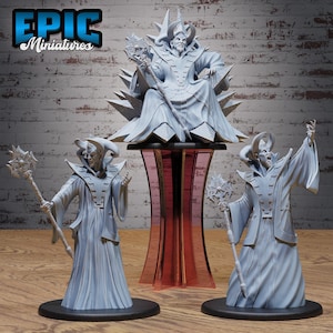 Puede incluir: Colección de figuras de fantasía de Epic Miniatures. La imagen presenta una figura sentada sobre un pedestal, flanqueada por dos figuras de pie, todas en color gris claro. Cada figura sostiene un bastón con una parte superior en forma de estrella, y el pedestal tiene un diseño de vidrio teñido de rojo.