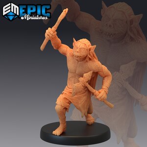 May include: A miniature figurine of a goblin-like creature with a club and an axe. The figure is painted in a light brown color and is standing on a black base.