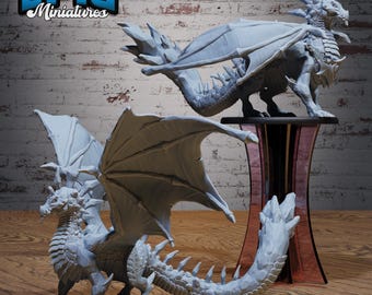May include: Two gray dragon miniatures with detailed wings, scales, and horns. One dragon stands on a clear, red-tinted display stand. The other dragon is on a black base. The text "EPIC Miniatures" is in the upper left corner.
