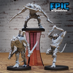 May include: Three gray painted miniature figures of humanoid creatures with animal features, holding weapons. The figures are posed in a dynamic action stance. The figures are on black bases and are displayed on a red and clear acrylic stand. The background is a white brick wall. The text "EPIC Miniatures" is in the upper right corner of the image.