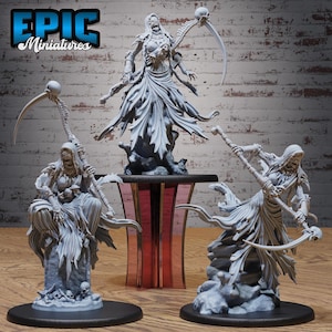 May include: Three grey miniature figurines of grim reapers with scythes and skull details. One figure stands atop a pedestal, while the others are posed on bases. The text "EPIC Miniatures" is in the upper left corner.