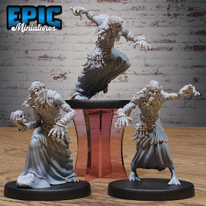 May include: Three grey miniature figures of a fantasy creature with long hair and flowing robes. One figure is posed mid-leap, while the others stand on black bases. The figures have detailed facial features and are posed with outstretched arms. The text "EPIC Miniatures" is in the upper left corner.