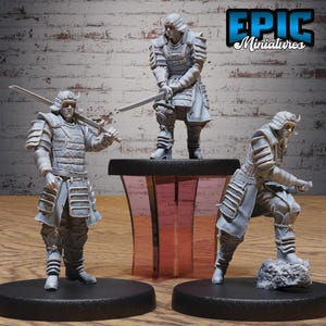 May include: Three gray miniature samurai figures in various action poses. One figure stands on a black base, holding a sword. Another stands on a table, and the third kneels on a rock. The Epic Miniatures logo is in the top right.