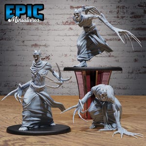 May include: Three gray miniature figures of skeletal creatures with long, claw-like fingers and horns. One figure stands on a black base, another on a pedestal, and the third is kneeling. The Epic Miniatures logo is in the upper left corner.
