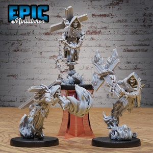 May include: Three gray painted miniature figures of skeletal figures in hooded robes, each holding a cross and chained, with flames around their feet. The figures are on black bases and a red base.