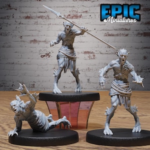 May include: Three grey unpainted fantasy creature miniatures on black circular bases. One figure stands holding a spear, another stands with arms outstretched, and the third crawls on the ground. Each figure features webbed limbs and rope belts.