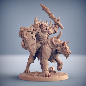May include: A miniature figurine of an Orc riding a wolf, both painted in a light brown color. The Orc is holding a sword in one hand and a shield in the other. The wolf has a fierce expression on its face.