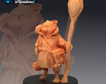 May include: A miniature figurine of a cat-like creature wearing a robe and holding a staff. The figurine is painted in a light brown colour and has a detailed design. The figurine is standing on a black base.