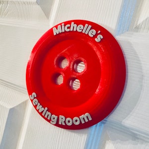 May include: Red button-shaped sign with white text that reads "Michelle's Sewing Room".