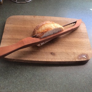 May include: A wooden bread knife with a serrated blade is being used to cut a loaf of bread on a wooden chopping board.