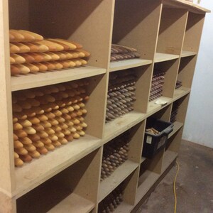 Op de afbeelding: Een houten plankenstel gevuld met stapels houten pinnen in verschillende tinten bruin en beige. De pinnen zijn netjes en georganiseerd gerangschikt, wat een visueel aantrekkelijk display cre&euml;ert.