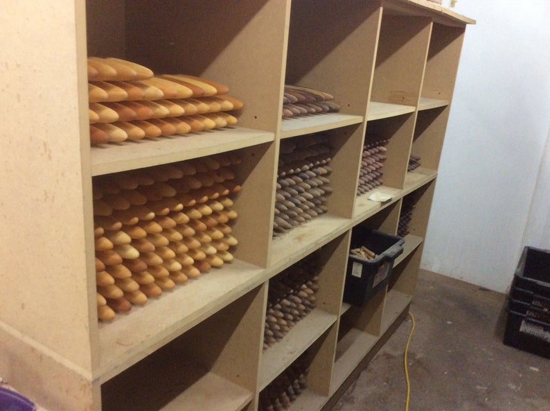 Op de afbeelding: Een houten plankenstel gevuld met stapels houten pinnen in verschillende tinten bruin en beige. De pinnen zijn netjes en georganiseerd gerangschikt, wat een visueel aantrekkelijk display cre&euml;ert.