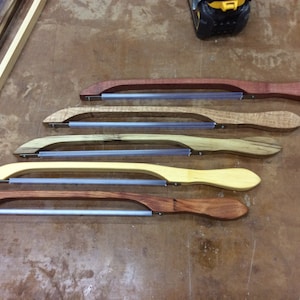 May include: Five wooden saw blades with clear plastic blades. The blades are of different lengths and have different wood grain patterns.