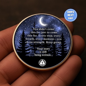 May include: A round, gold-toned coin featuring a night sky scene with a crescent moon, stars, and silhouetted trees. The coin has inspirational text: "You didn't come this far... Keep going. Your story is still being written..."