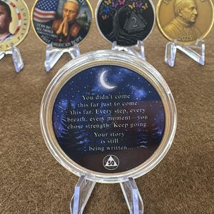 May include: A collection of commemorative coins displayed on clear stands. The coins feature various designs, including portraits, flags, and inspirational quotes. One coin has the text "You didn't come this far just to come..." and a crescent moon.