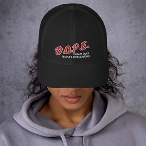 May include: Black mesh trucker hat with a red embroidered logo that says "D.O.P.E. DREAM OVER PEOPLE'S EXPECTATIONS"