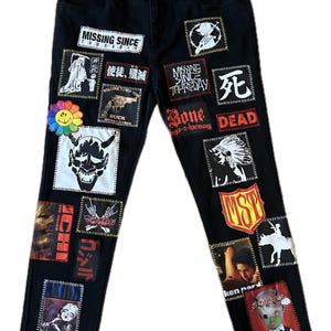 Könnte beinhalten: Schwarze Jeans aus Denim mit einer Vielzahl rechteckiger Aufnäher mit verschiedenen grafischen Drucken, darunter Texte wie "MISSING SINCE THURSDAY", "DEAD" und "ICHI" sowie Abbildungen einer Dämonenmaske, eines Totenkopfes und einer bunten Blume.