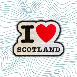 May include: White embroidered patch with the text "I love Scotland" in black lettering. A red heart is between the "I" and the word "Scotland".