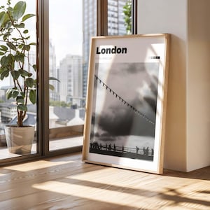 Puede incluir: Una fotografía en blanco y negro enmarcada de un puente con gente caminando por él. El texto "London, England, UK" está impreso en la parte superior de la foto.