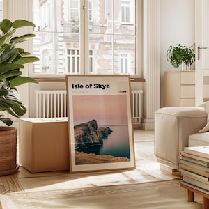 May include: A framed poster with a photograph of a rocky coastline and the text "Isle of Skye, Scotland, UK". The poster is leaning against a cardboard box in a room with a large window and a white couch.