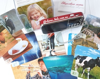 May include: A set of colorful flashcards with various images, including a girl, a lion, a cup of coffee, a vacuum cleaner, a whale, a cow, a trumpet, and a woodpecker. The cards are numbered and have a speaker with a red and black design. The text on the speaker says "@clever_kids.com.ua".